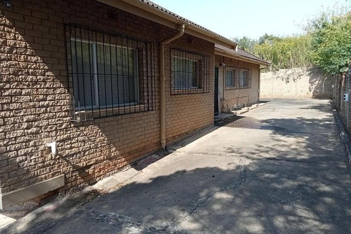 Rear exterior view of a face brick house featuring a concrete driveway, security bars on windows, and a perimeter boundary wall.