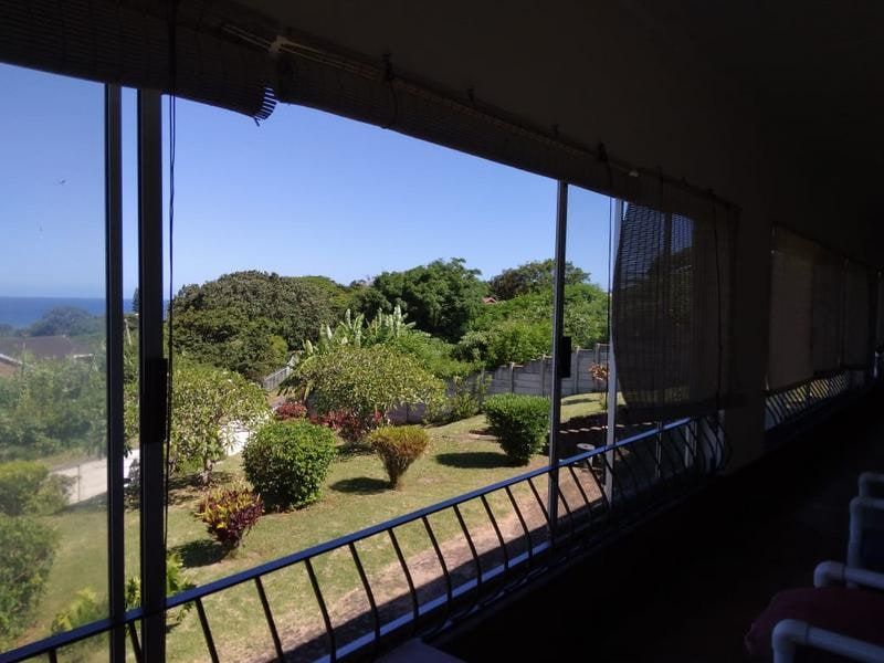 A covered balcony area featuring large sliding glass doors, metal safety railings, and bamboo blinds, offering an elevated view of the garden and landscape.