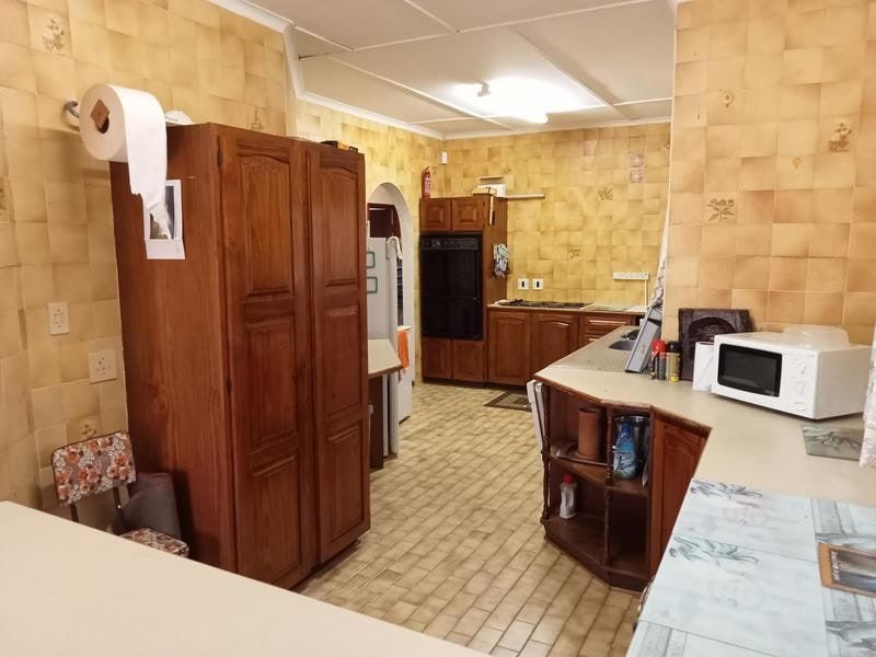 A dated kitchen featuring extensive wall tiling, built-in cabinetry, and a breakfast bar, offering significant potential for a modern renovation.