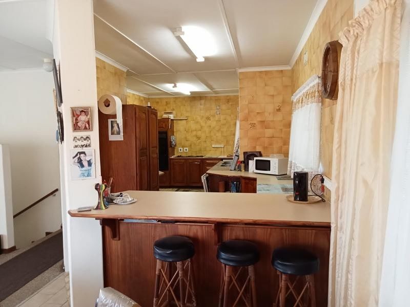 A dated kitchen featuring timber cabinetry, a breakfast bar, and tiled splashbacks, offering significant potential for a modern renovation.
