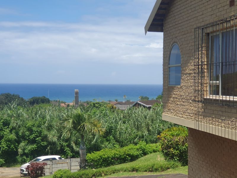A scenic view of the ocean from the side of a brick residential property featuring an arched window and security bars.