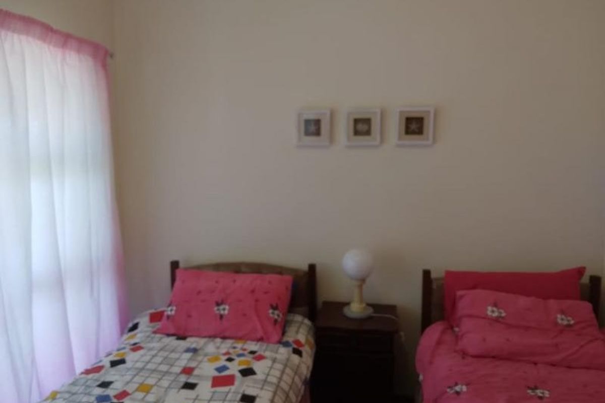 A bedroom featuring two single beds with a central bedside table and window with curtains.