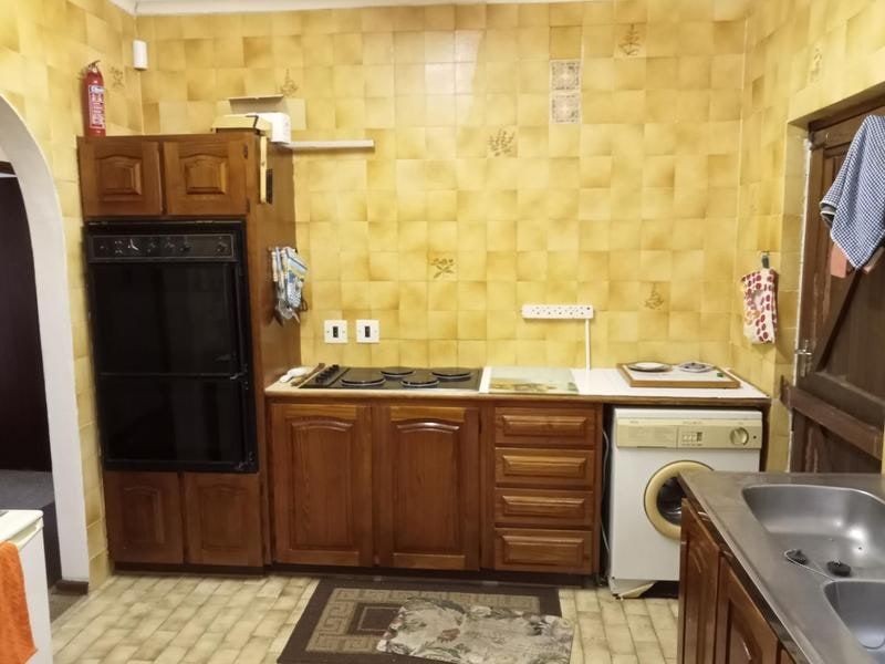 A dated kitchen featuring wooden cabinetry, a built-in oven, electric hob, and tiled wall finishes, offering significant potential for a modern renovation.