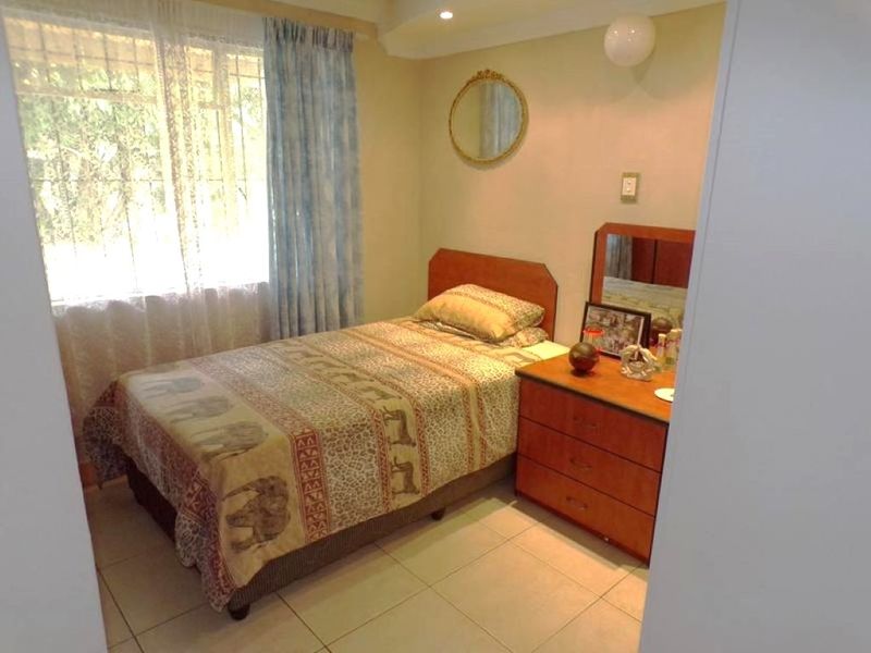 A functional bedroom featuring tiled flooring, recessed lighting, and security bars on the window, providing a comfortable and secure living space.