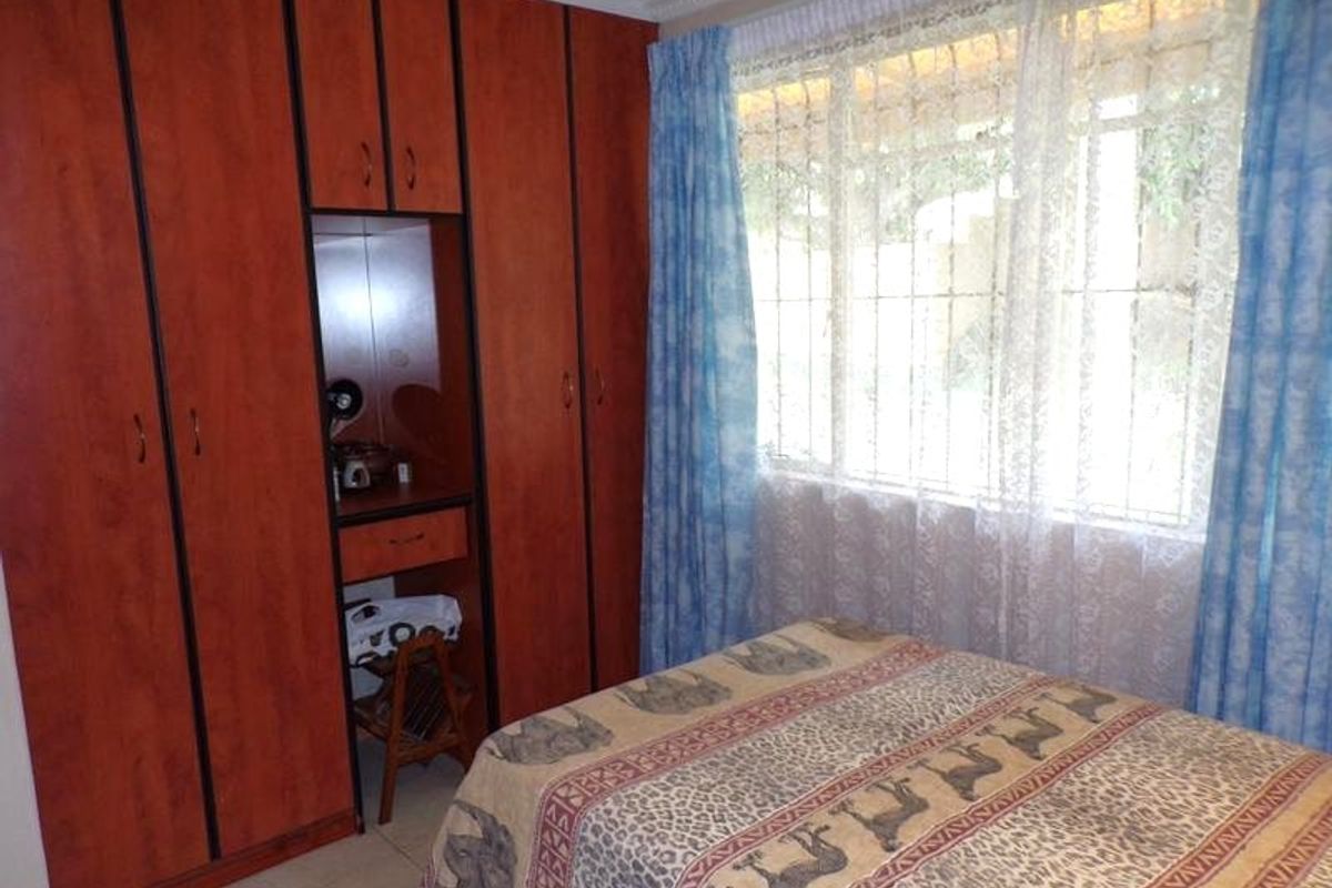 A bedroom featuring built-in wooden cupboards with an integrated vanity area, tiled flooring, and a window fitted with security bars.