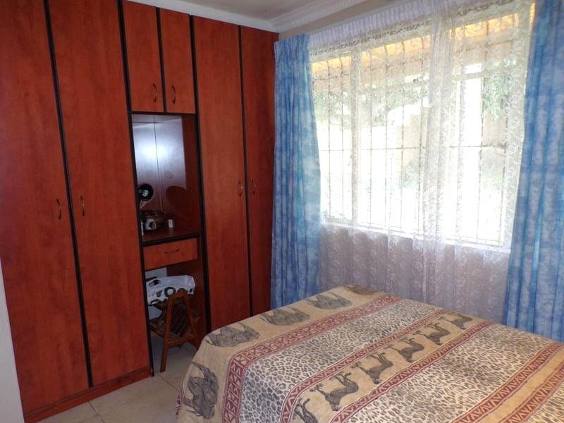 A bedroom featuring built-in wooden cupboards with an integrated vanity area, tiled flooring, and a window fitted with security bars.