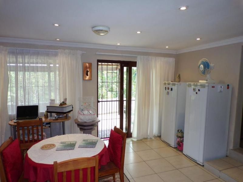 A functional living area featuring ceramic tiled flooring, recessed downlighting, and a sliding glass door with a security gate leading to the exterior.