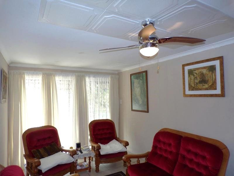 A living room featuring a tiled ceiling, ceiling fan, and tiled flooring with large windows covered by curtains.