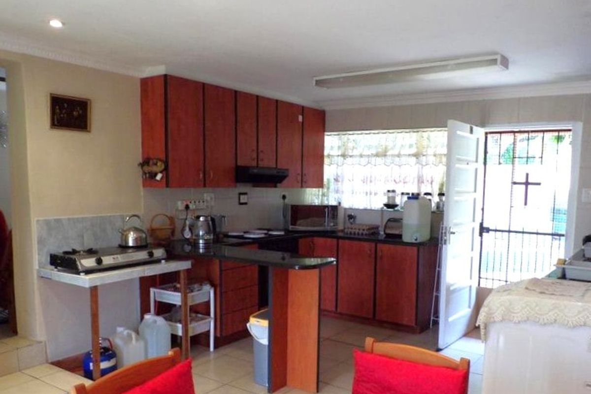 A functional kitchen featuring wood-tone cabinetry, dark countertops, tiled flooring, and direct access to the exterior via a security gate.