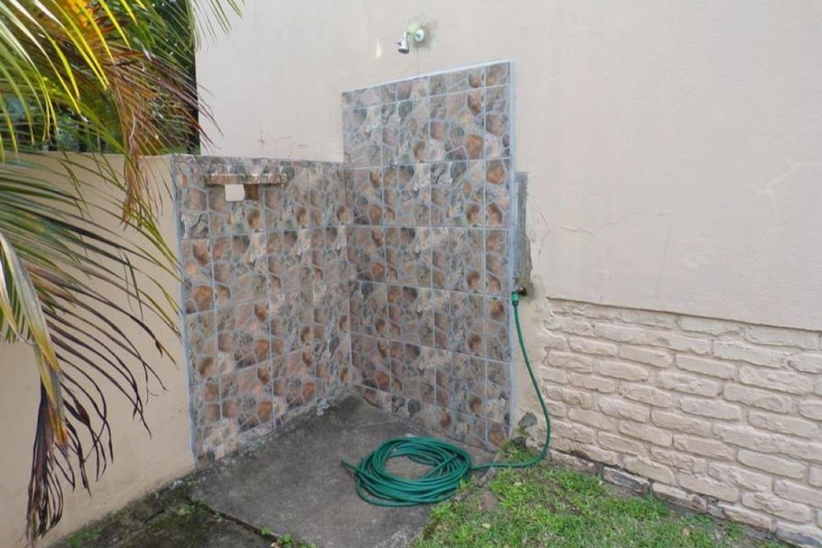 An outdoor shower area featuring a tiled splashback and concrete base, located against the rear exterior wall of the townhouse.