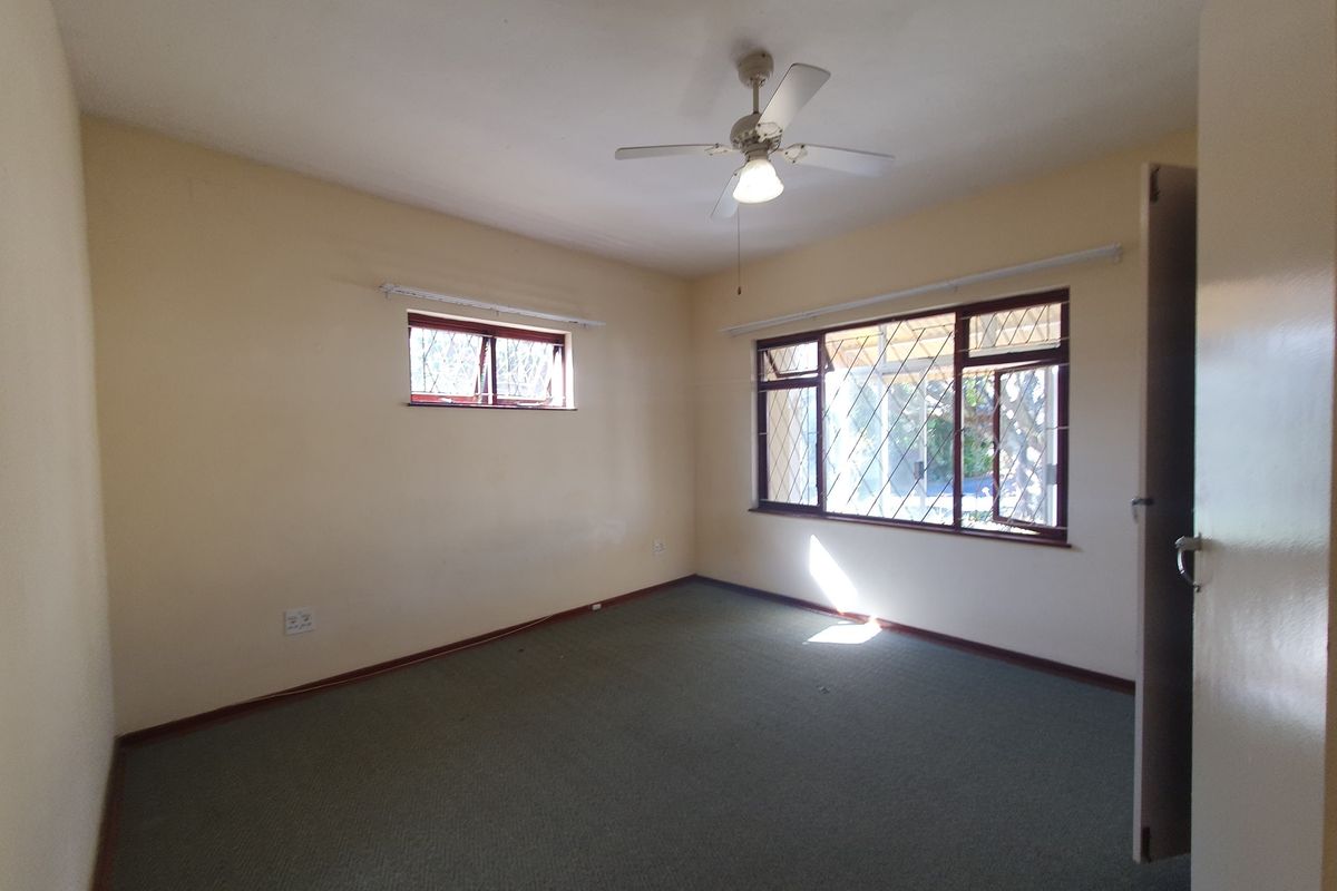 A vacant bedroom featuring carpet flooring, a ceiling fan, and windows fitted with security bars.