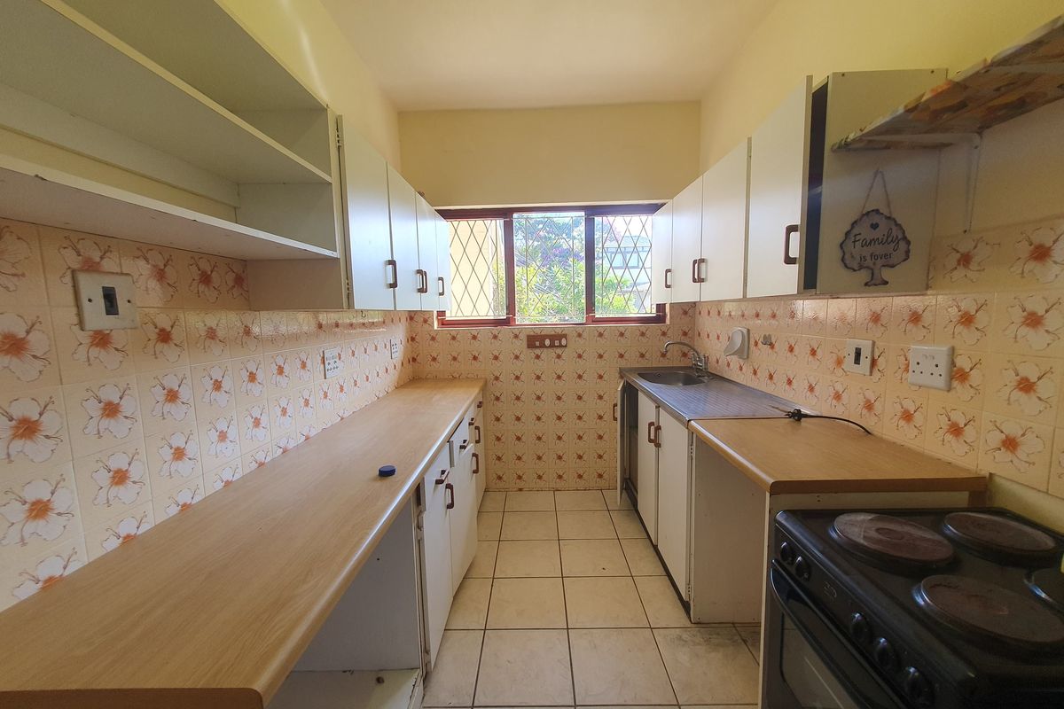 A dated kitchen featuring laminate countertops, ceramic wall tiles, and built-in cabinetry, offering a functional layout with potential for modern renovation.
