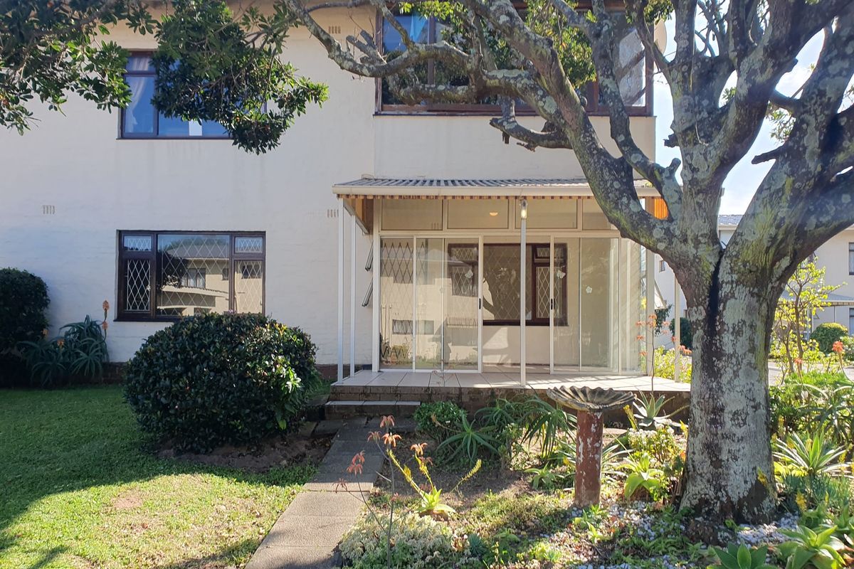 Rear view of the apartment building featuring an enclosed patio area, concrete walkway, and established garden surroundings.