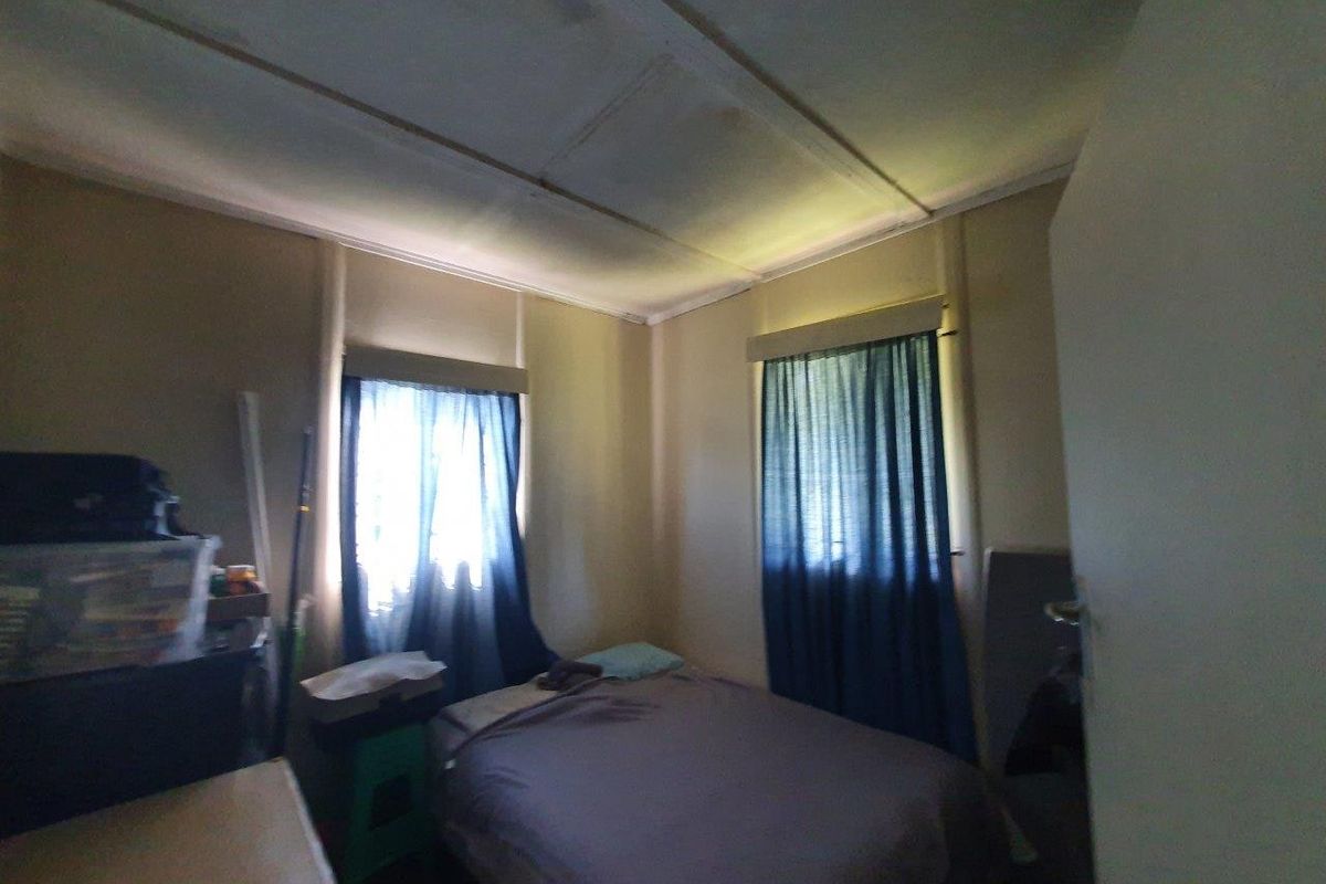 A compact bedroom featuring two windows and standard ceiling paneling, requiring cosmetic updates to improve the overall finish and appeal.