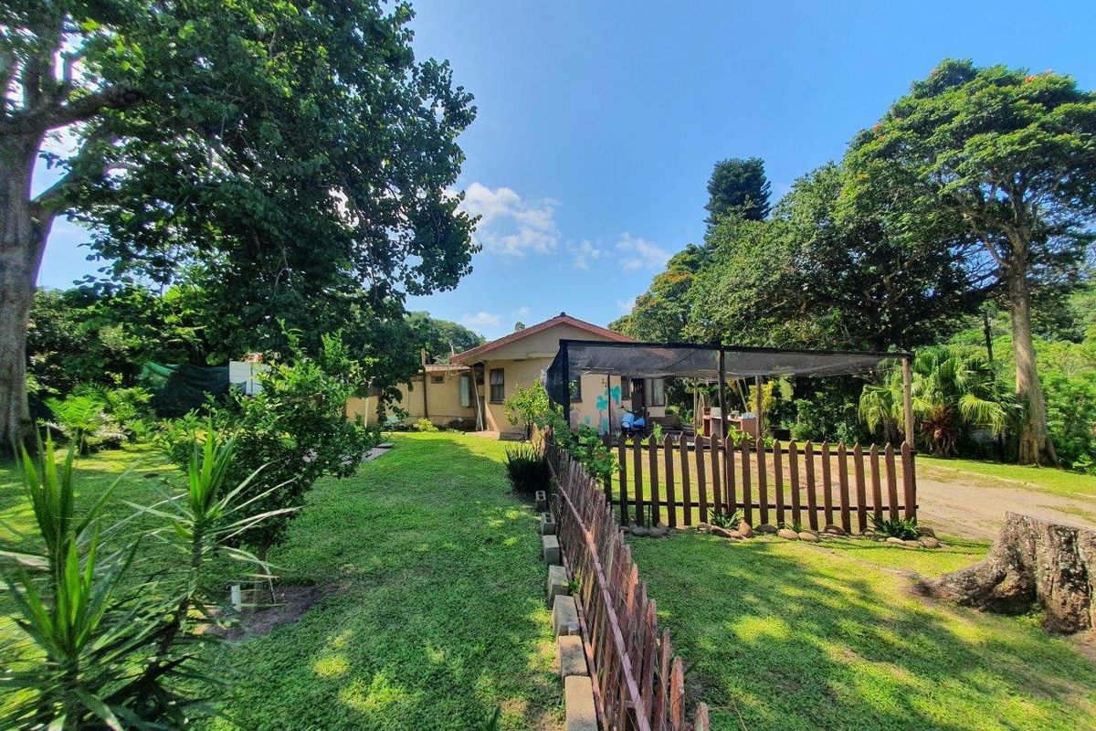 A view of the rear garden featuring a timber picket fence, a shaded outdoor area, and established trees on a spacious lawn.