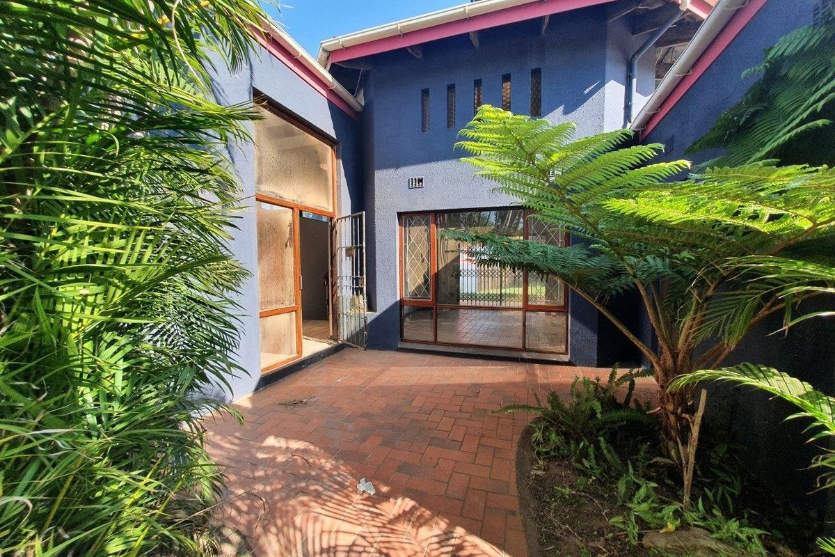 A rear courtyard featuring brick paving, established garden greenery, and access to the home through sliding glass doors and a security gate.