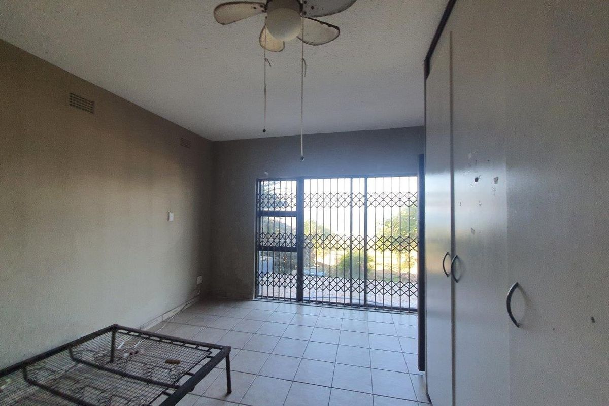A bedroom featuring tiled flooring, built-in cupboards, a ceiling fan, and a sliding door with a security gate leading to the exterior.