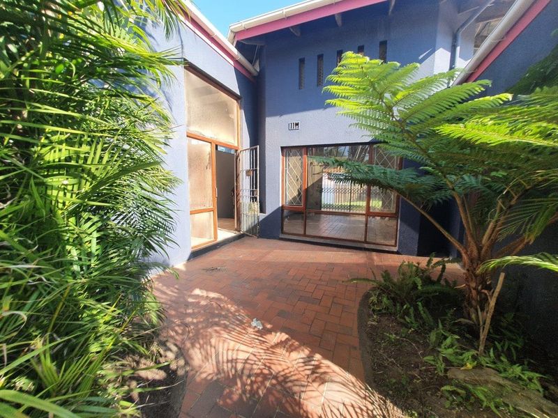A paved outdoor patio area featuring blue exterior walls, large glass windows, and a security gate, providing a private transition space to the home interior.