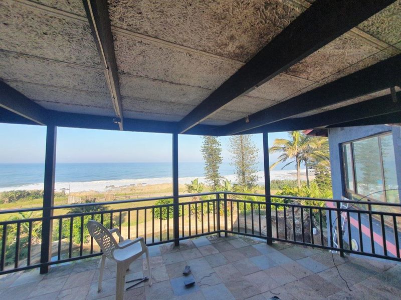 A covered outdoor patio featuring tiled flooring and a metal balustrade, offering expansive, unobstructed views of the ocean and coastline.