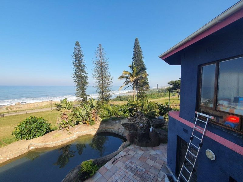 Elevated view overlooking the coastline, featuring a rock-lined swimming pool, tiled patio area, and direct ocean vistas.