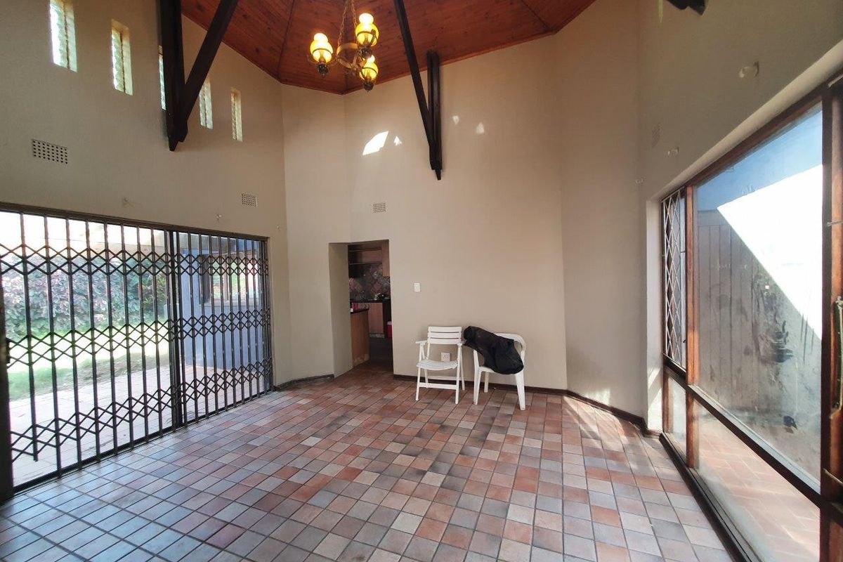 Spacious living area featuring a high vaulted timber ceiling with exposed beams, tiled flooring, and large sliding glass doors providing ample natural light.