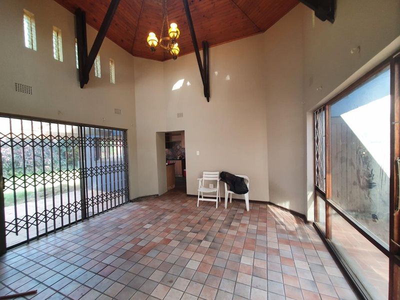 Spacious living area featuring a high vaulted timber ceiling with exposed beams, tiled flooring, and large sliding glass doors providing ample natural light.
