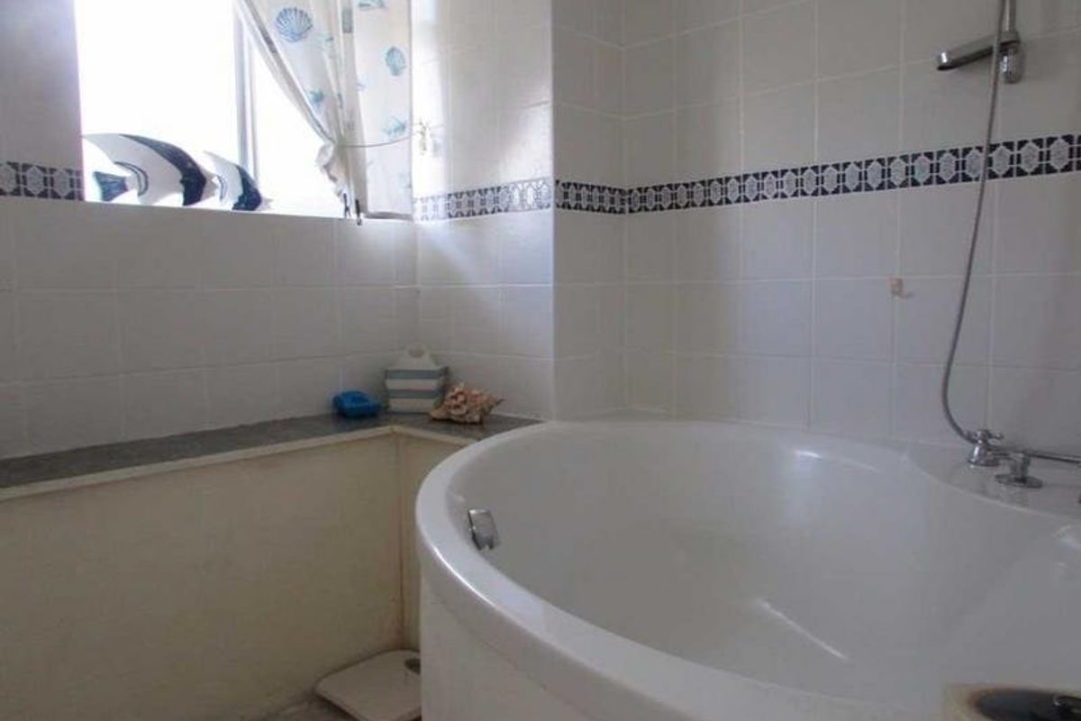 A functional bathroom featuring a corner bathtub, wall-mounted shower fixture, and tiled walls with a decorative border.