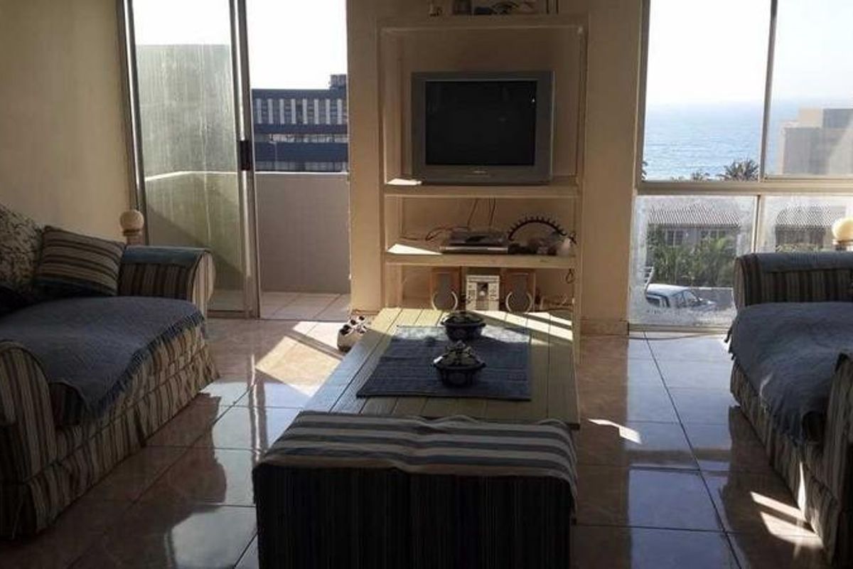 A living room featuring tiled flooring, built-in shelving, and large windows with natural light and ocean views, leading to a balcony.