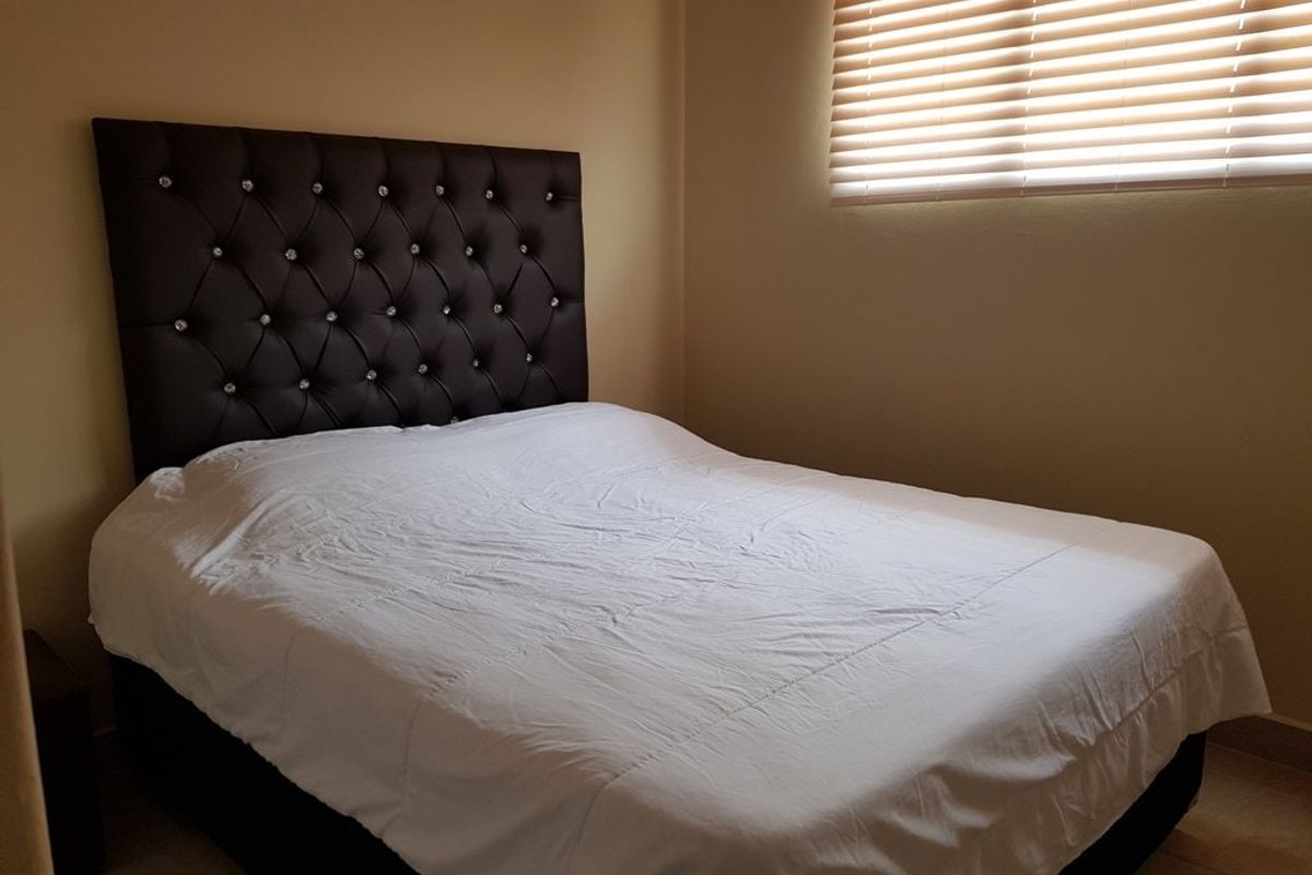 A functional bedroom featuring neutral wall tones and fitted venetian blinds, providing a simple and comfortable sleeping space.