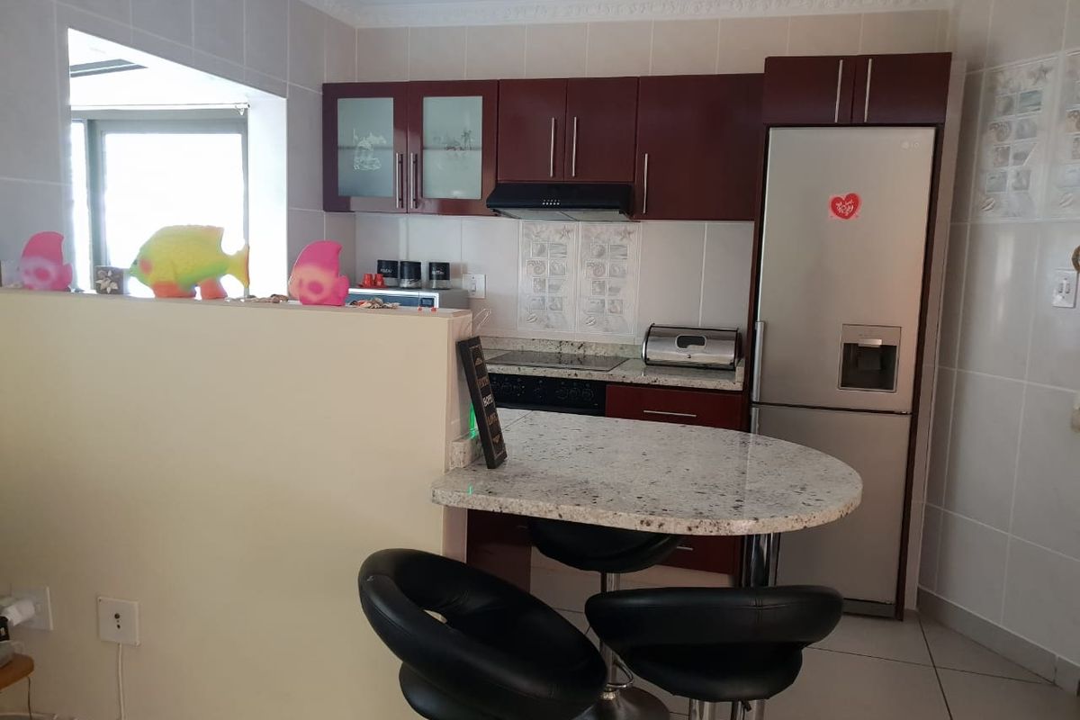 A compact kitchen featuring dark wood cabinetry, a granite breakfast bar, and tiled finishes, offering a functional layout for apartment living.