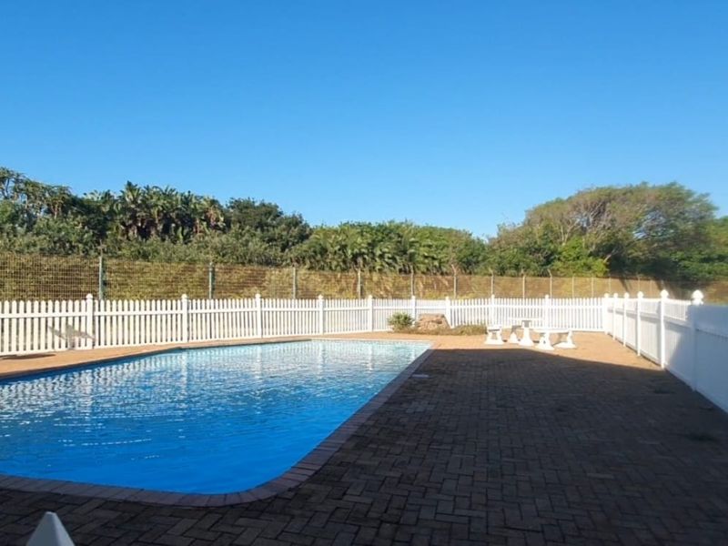A well-maintained outdoor swimming pool area featuring paved surrounds and a secure white picket fence enclosure.