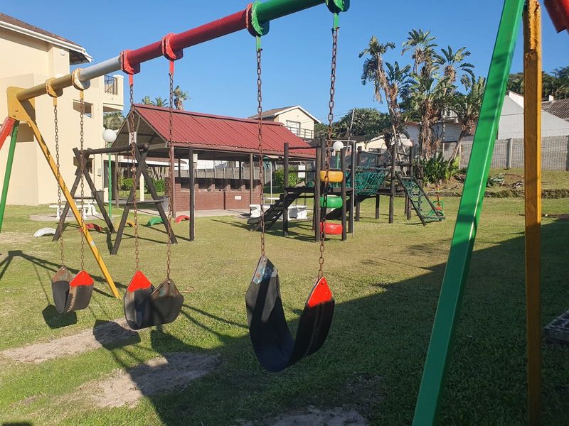 Communal garden area featuring a playground with swings and climbing frames, alongside a covered outdoor seating and braai area for residents.