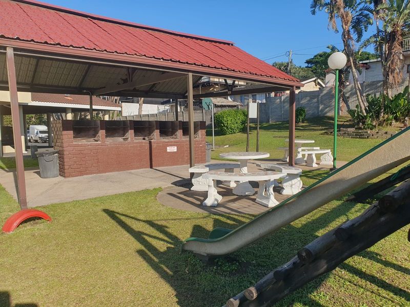 Communal outdoor area featuring a covered brick braai facility, paved seating space, and a garden with playground equipment.