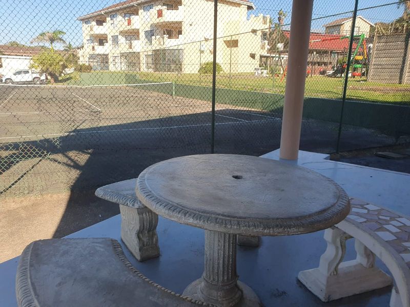 Covered patio area overlooking a communal tennis court, featuring concrete flooring and structural support pillars.