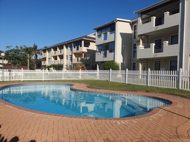 A well-maintained communal swimming pool area with brick paving and a white picket fence, set against the backdrop of apartment building balconies.