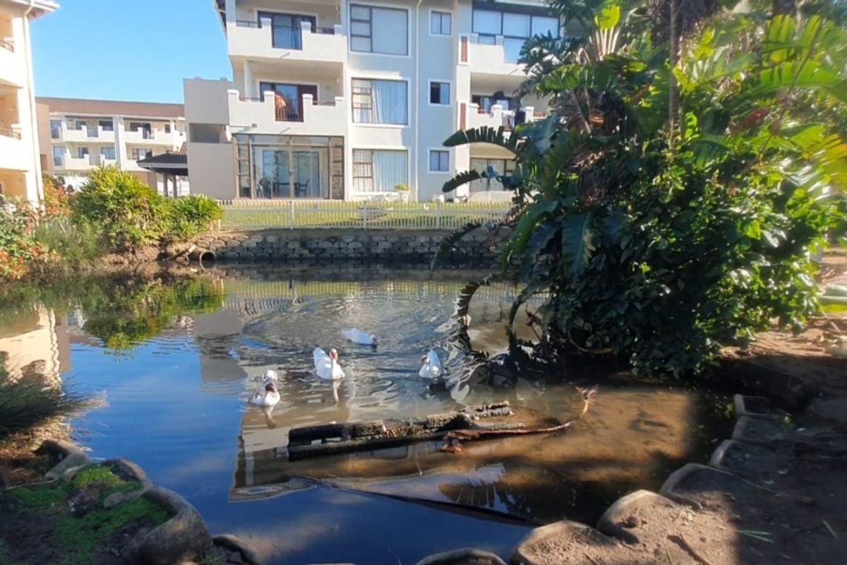 A view of the rear exterior of the apartment complex featuring a landscaped pond area with a stone retaining wall and white picket fencing.
