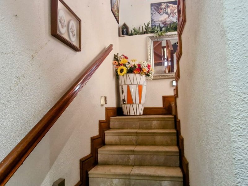 A narrow staircase featuring tiled steps and a wooden handrail, showing signs of wear on the surrounding wall surfaces.