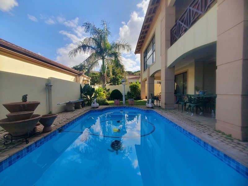 A private swimming pool area featuring a covered patio, paved surround, and a multi-story townhouse exterior with a balcony.