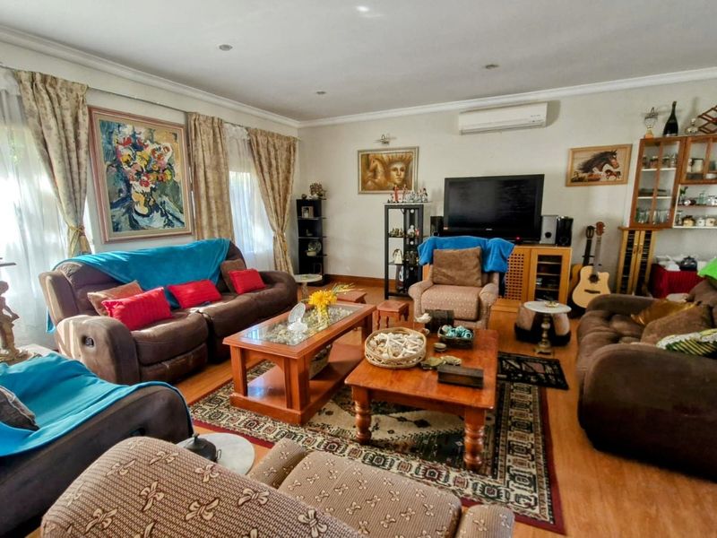 A spacious living room featuring laminate flooring, recessed downlighting, and a wall-mounted split-system air conditioning unit.