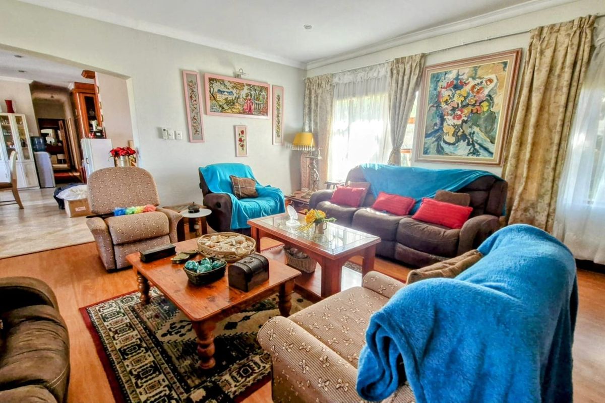 A spacious living room featuring laminate flooring, coved cornicing, and recessed downlights, with an open-plan flow leading into the adjacent dining area.