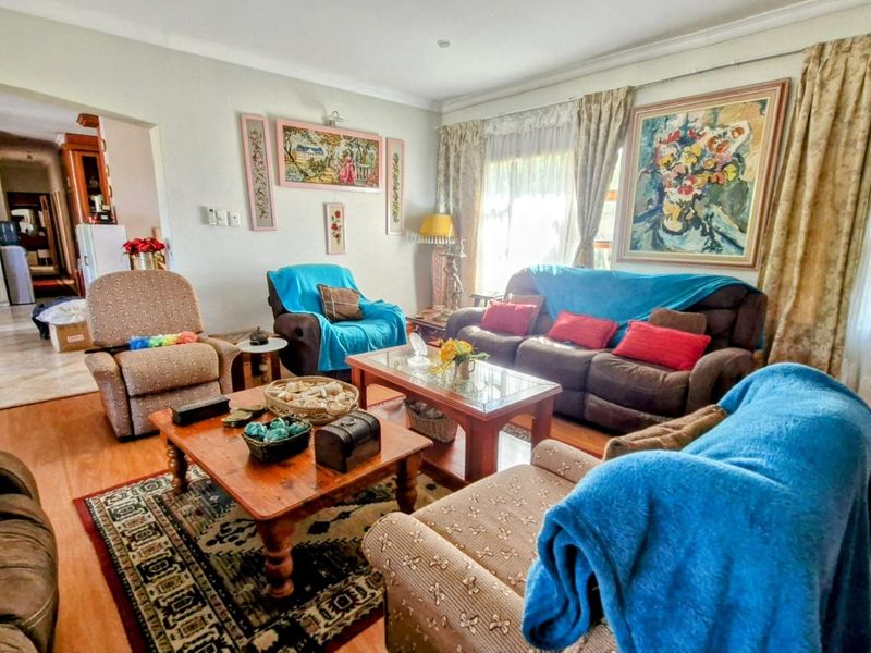 A spacious living room featuring laminate flooring, coved cornicing, and recessed downlights, with an open-plan flow leading into the adjacent dining area.
