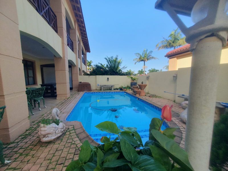 Outdoor pool area featuring a swimming pool, brick paved surround, and a covered patio area attached to the townhouse structure.