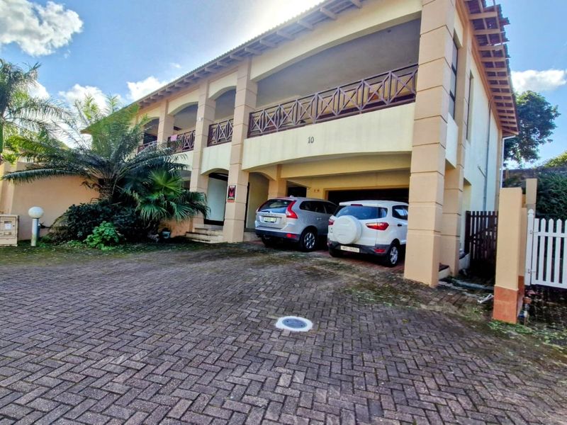 Front elevation of a two-story townhouse featuring a paved driveway, integrated double garage, and an upper-level balcony with timber balustrades.