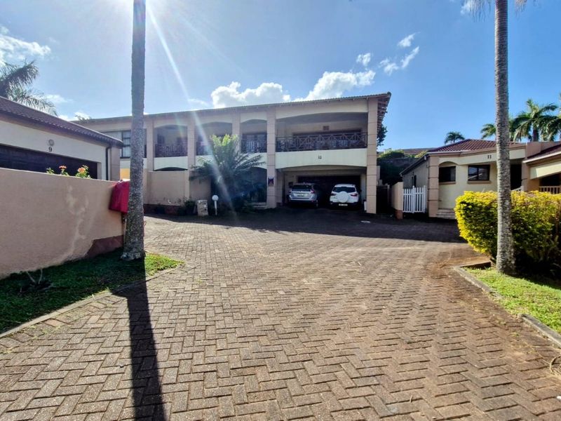 Front exterior view of a townhouse complex featuring a paved driveway, covered parking bays, and upper-level balconies.