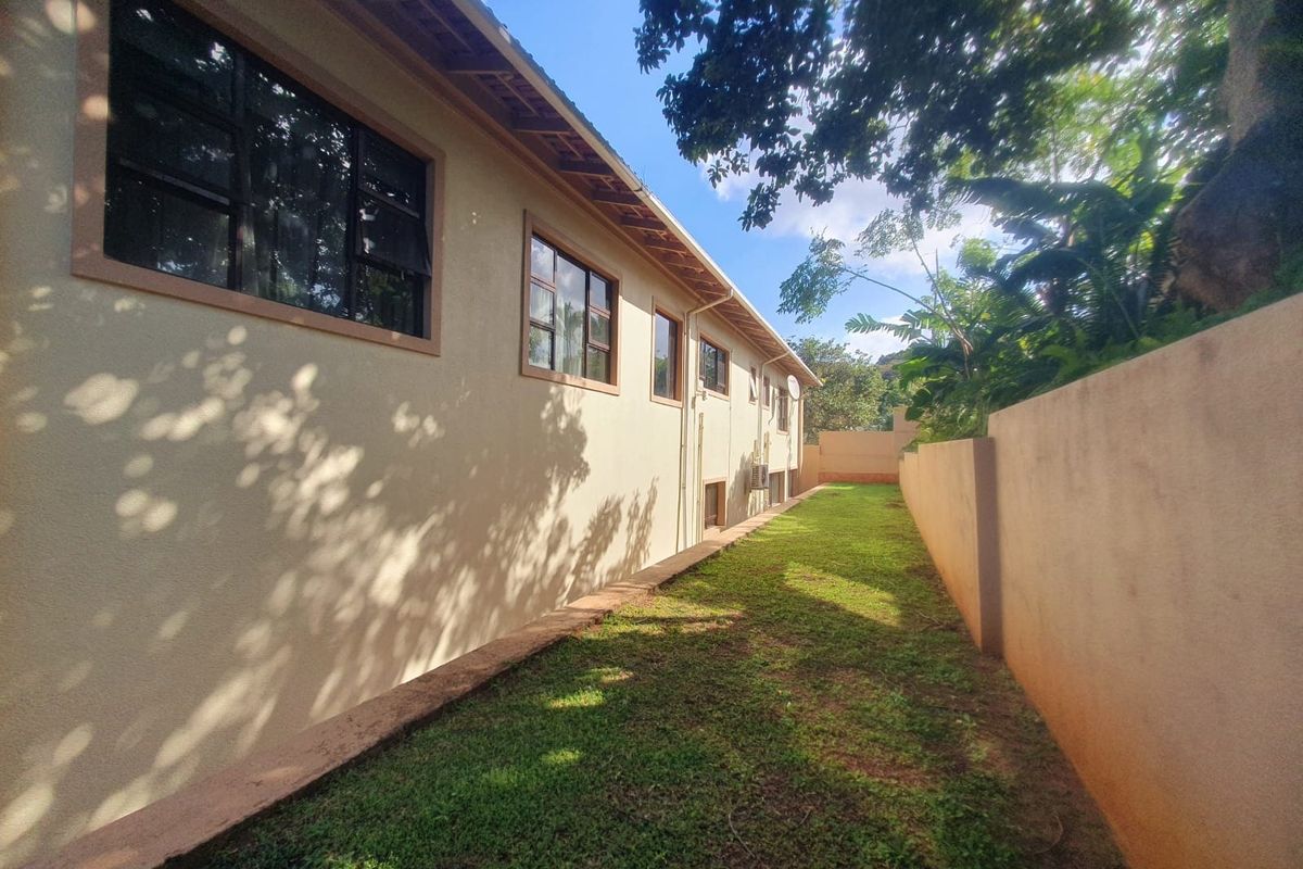 A view of the rear exterior of the townhouse, featuring a side garden path, perimeter boundary wall, and multiple casement windows along the building facade.
