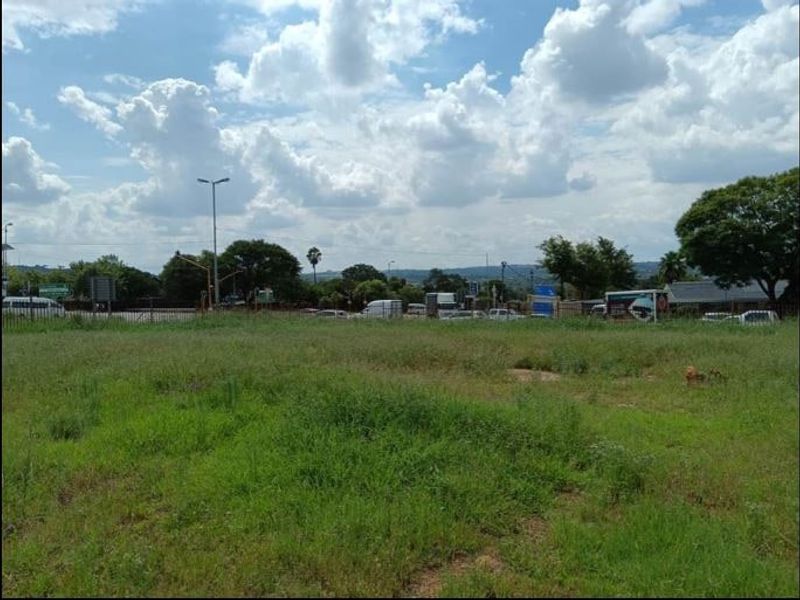 A vacant residential land plot featuring open grass area with perimeter fencing and street-level access.