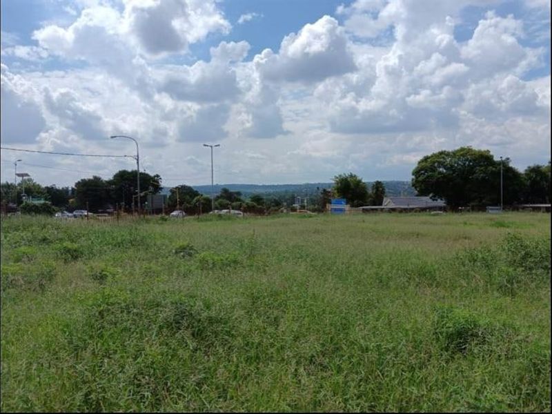 A vacant residential plot of land featuring open grass coverage with surrounding street infrastructure and distant neighborhood views.