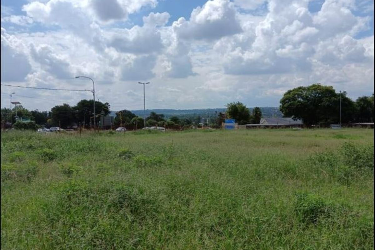 A vacant residential plot of land featuring open grass coverage with surrounding street infrastructure and distant neighborhood views.