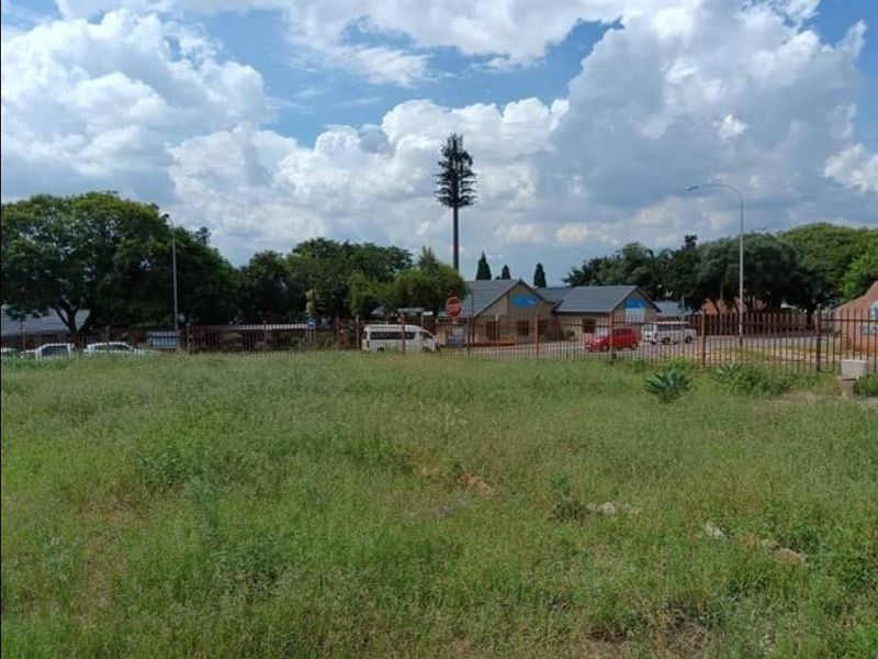 A vacant residential plot featuring natural grass cover and metal perimeter fencing, situated in a developed neighborhood setting.