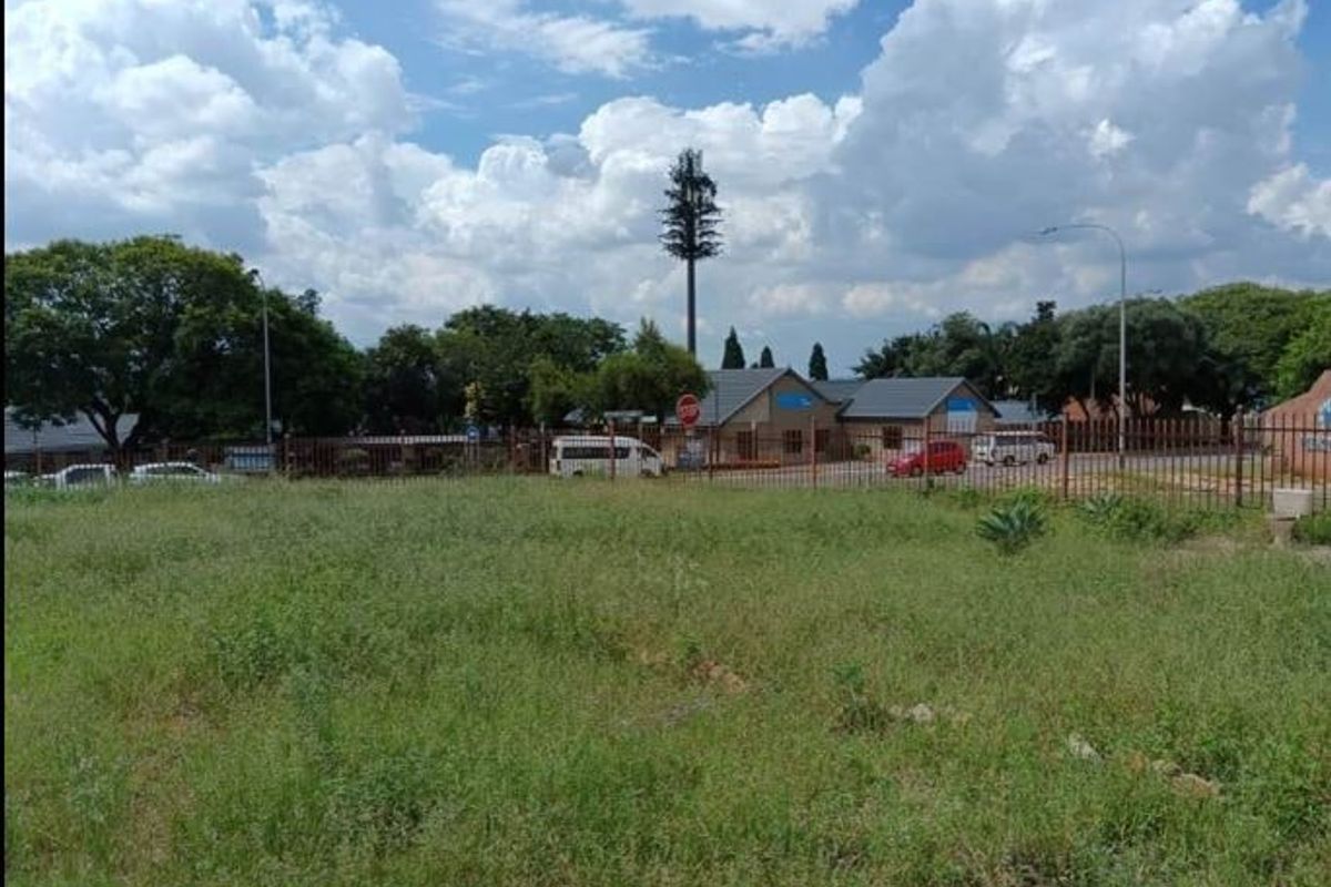 A vacant residential plot featuring natural grass cover and metal perimeter fencing, situated in a developed neighborhood setting.